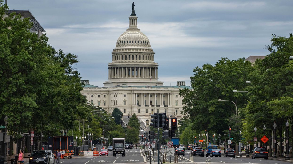US Capitol building with cars on street flanked by trees in foreground.