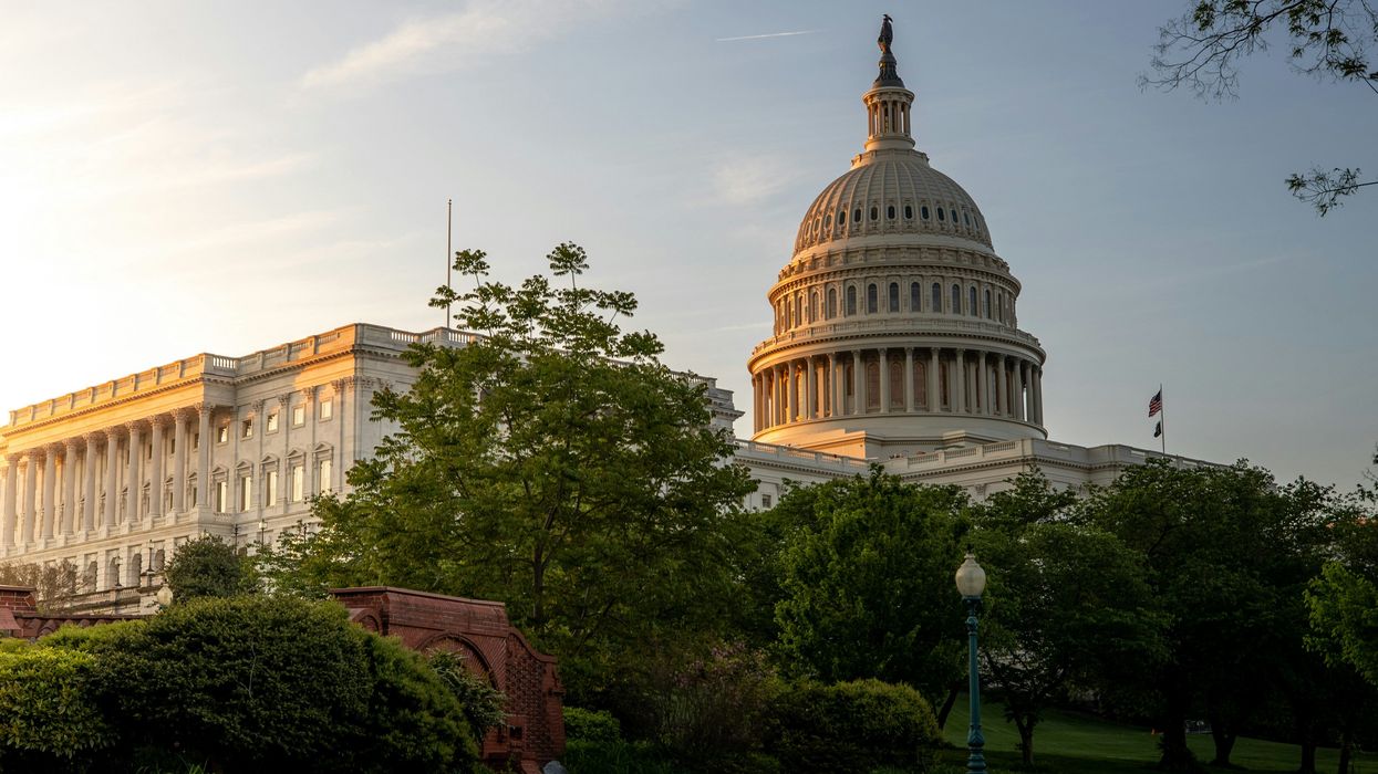 US Capitol dome touched by early morning sun with trees and a path in foreground.