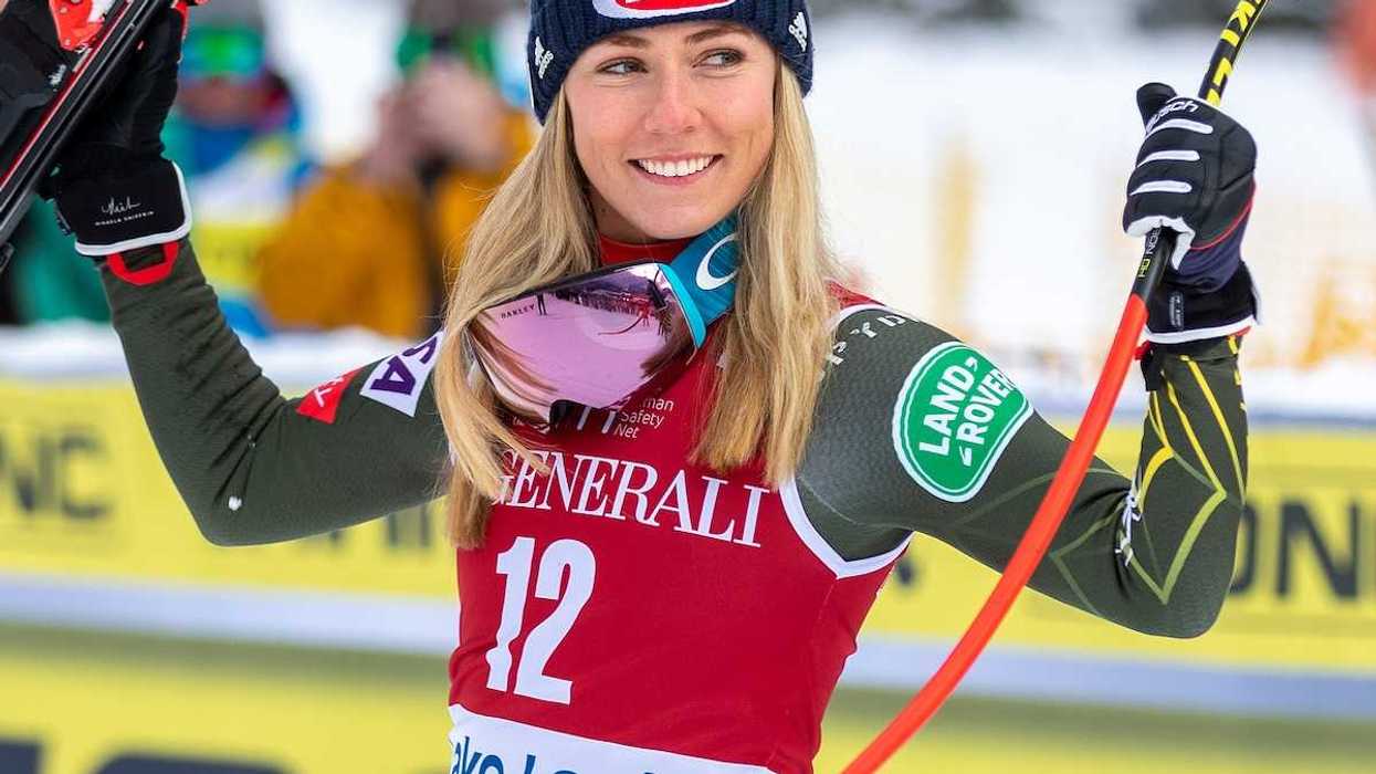 US skier Michaela Shiffrin in red bib holding skis and pole at finish
