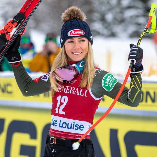 US skier Michaela Shiffrin in red bib holding skis and pole at finish