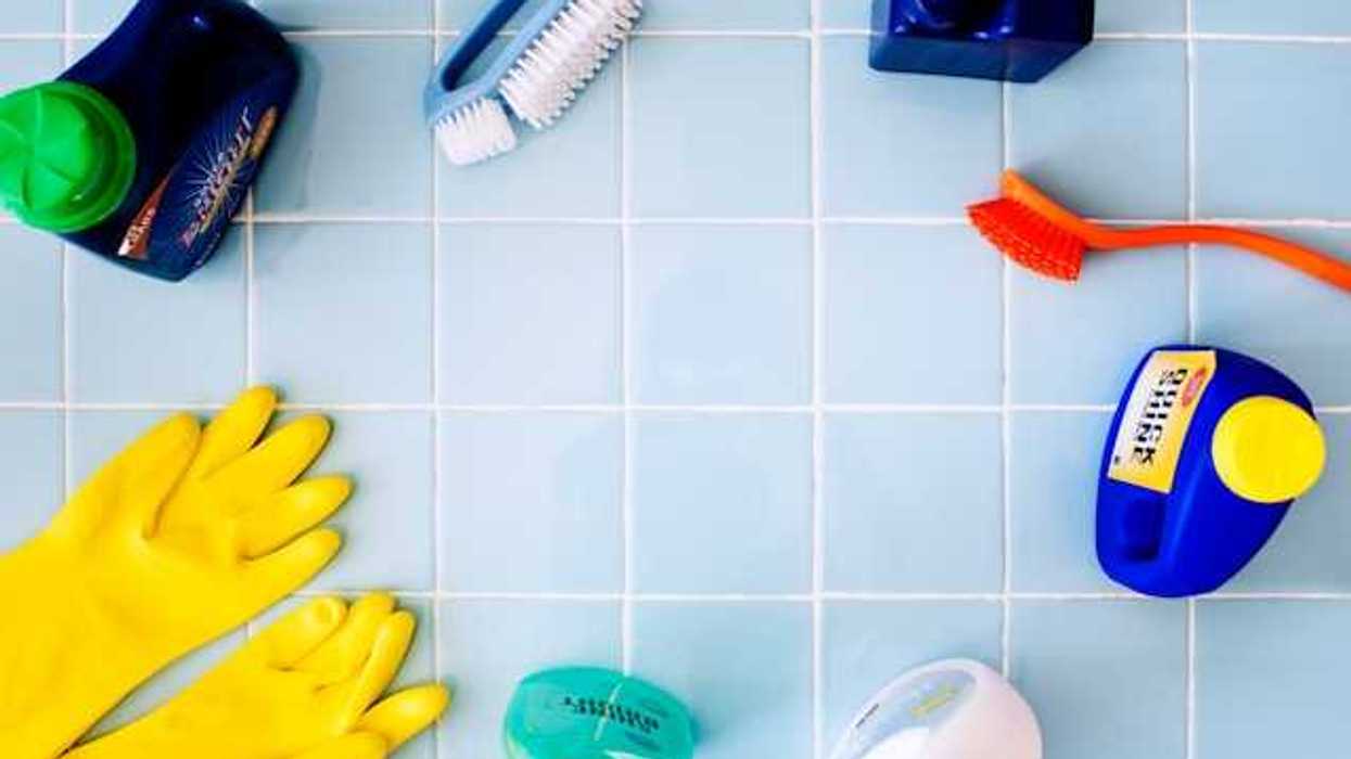 Various bathroom cleaning products, sprays, and tools laid out on a blue tile floor