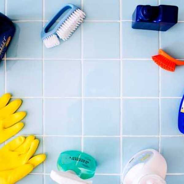 Various bathroom cleaning products, sprays, and tools laid out on a blue tile floor