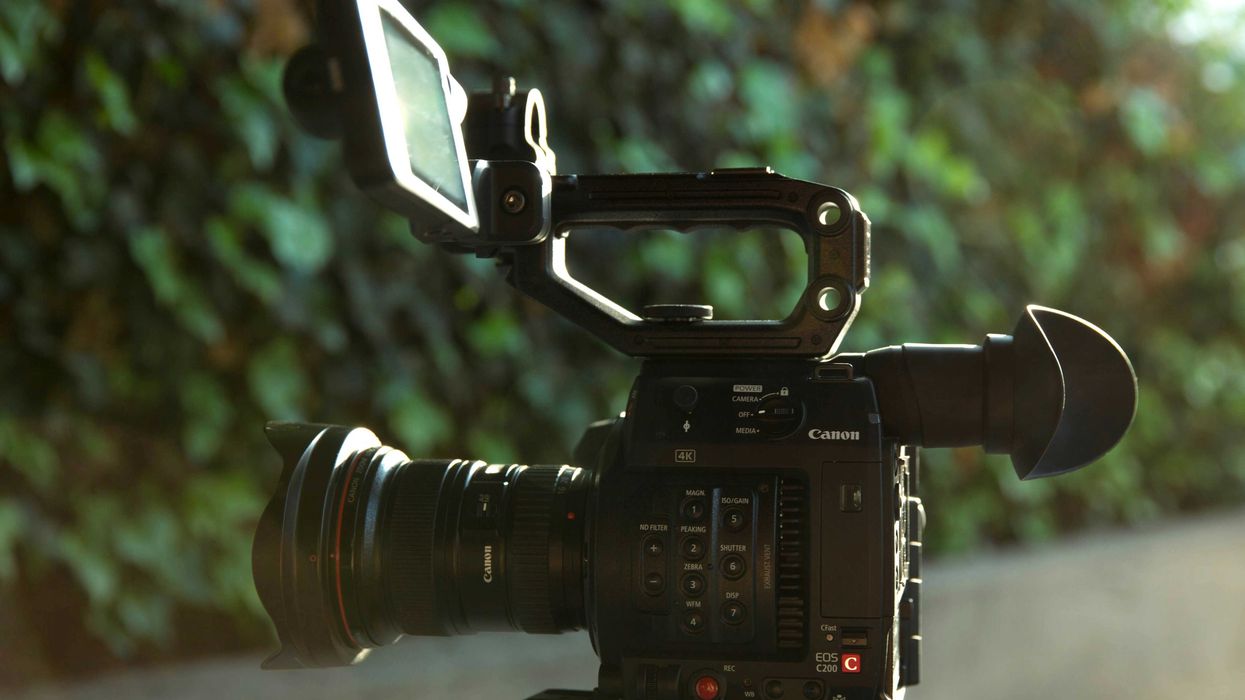 Video camera on a tripod facing a green hedge.