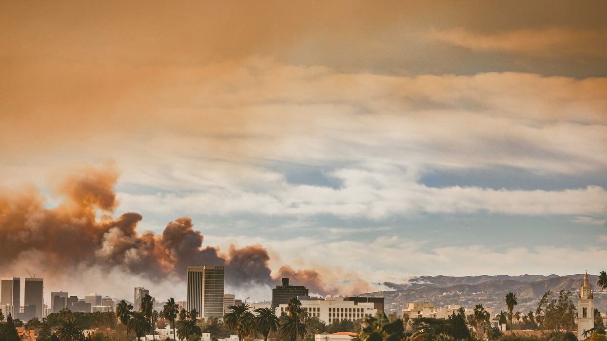 View of a wildfire on hills behind Los Angeles emitting dark smoke into the air.