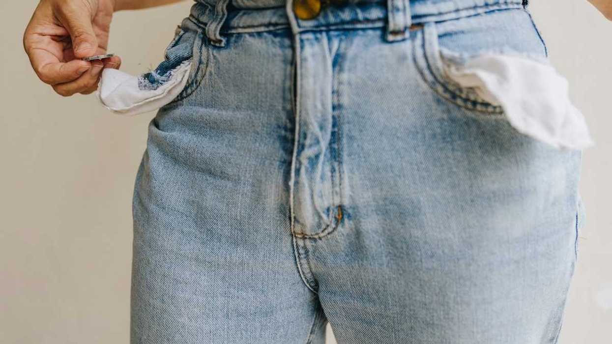 Waist-down shot of person retrieving a single coin from inside-out pockets of worn blue jeans