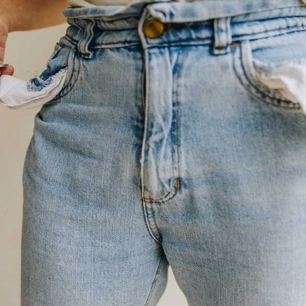 Waist-down shot of person retrieving a single coin from inside-out pockets of worn blue jeans