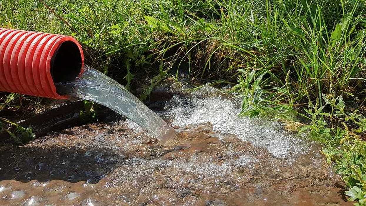 Water flowing from a red pipe into the ground