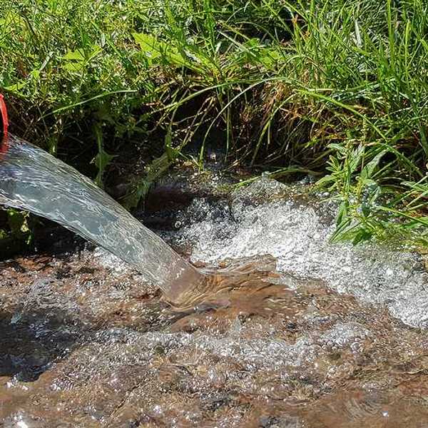 Water flowing from a red pipe into the ground