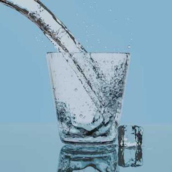 Water pouring into a glass from the left, with an ice cube sitting to the right