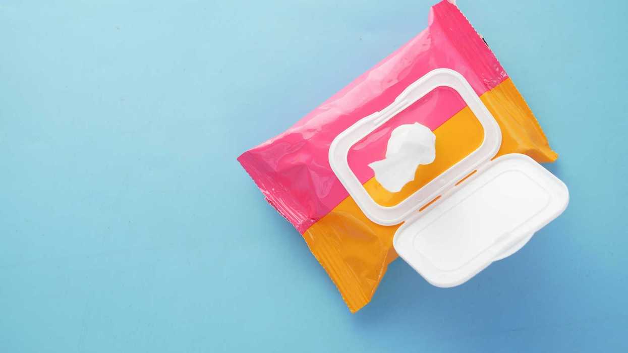 Wet wipes in a pink and orange container against blue surface.