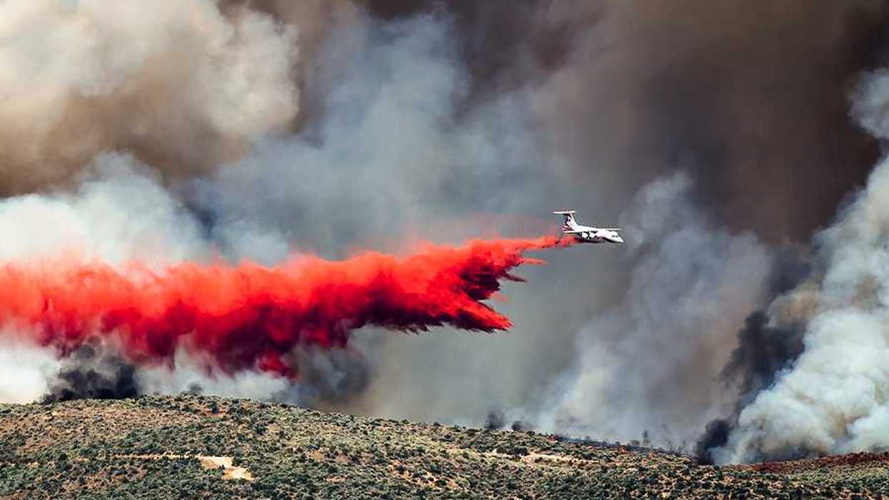 White aircraft dropping fire retardant as it battles the raging wildfire