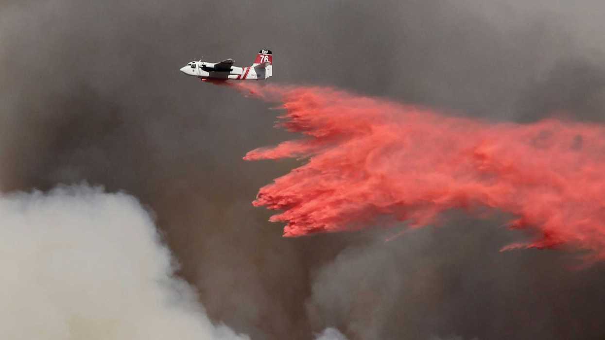 white and red airplane pouring red powder on fire with dark smoke in background.