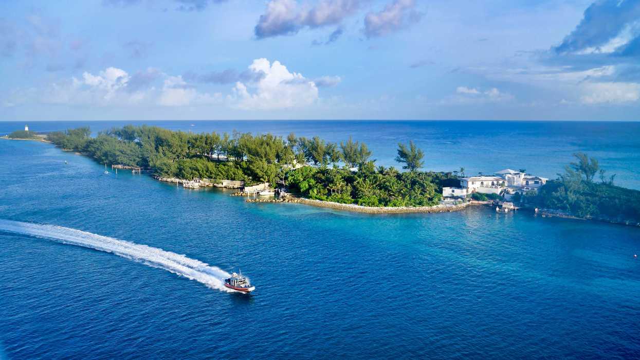 white boat on sea under blue sky during daytime with a small tree-covered island in background.