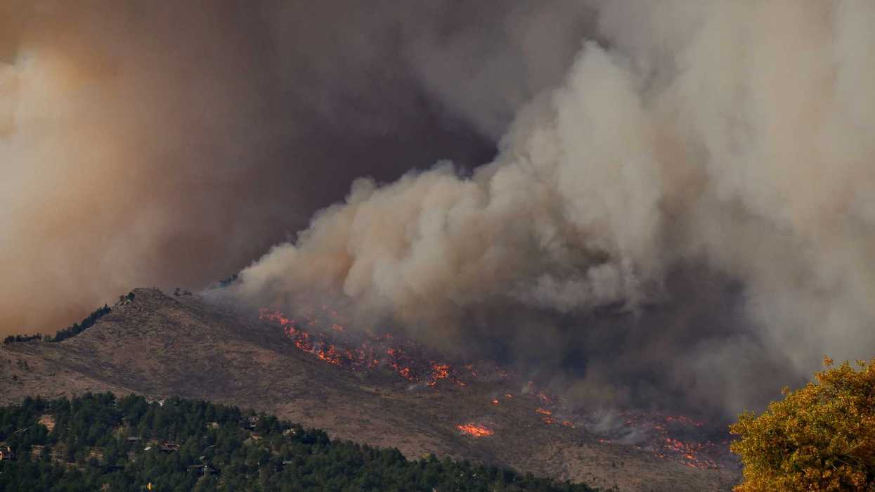 wildfire burning on a ridge with gray smoke billowing.