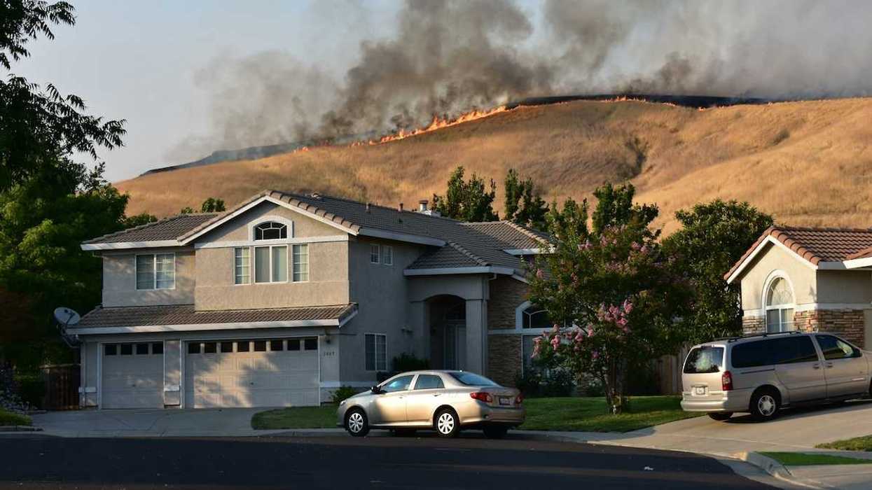 Wildfire on ridgetop threatens a neighborhood. Suburban home with vehicles in driveway.
