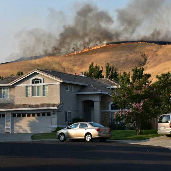 Wildfire on ridgetop threatens a neighborhood. Suburban home with vehicles in driveway.