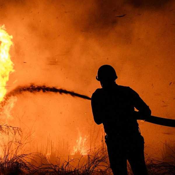 Wildland fire fighter, silhouetted against flame-orange backdrop, training hose on wildfire.