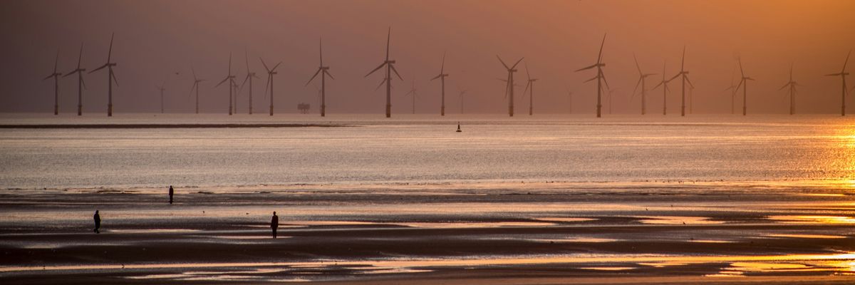 Wind turbines in the ocean in a row off a beach at sunset.