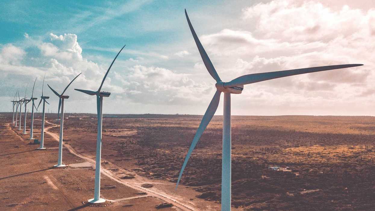 wind turbines on brown sand under white clouds and blue sky during daytime.