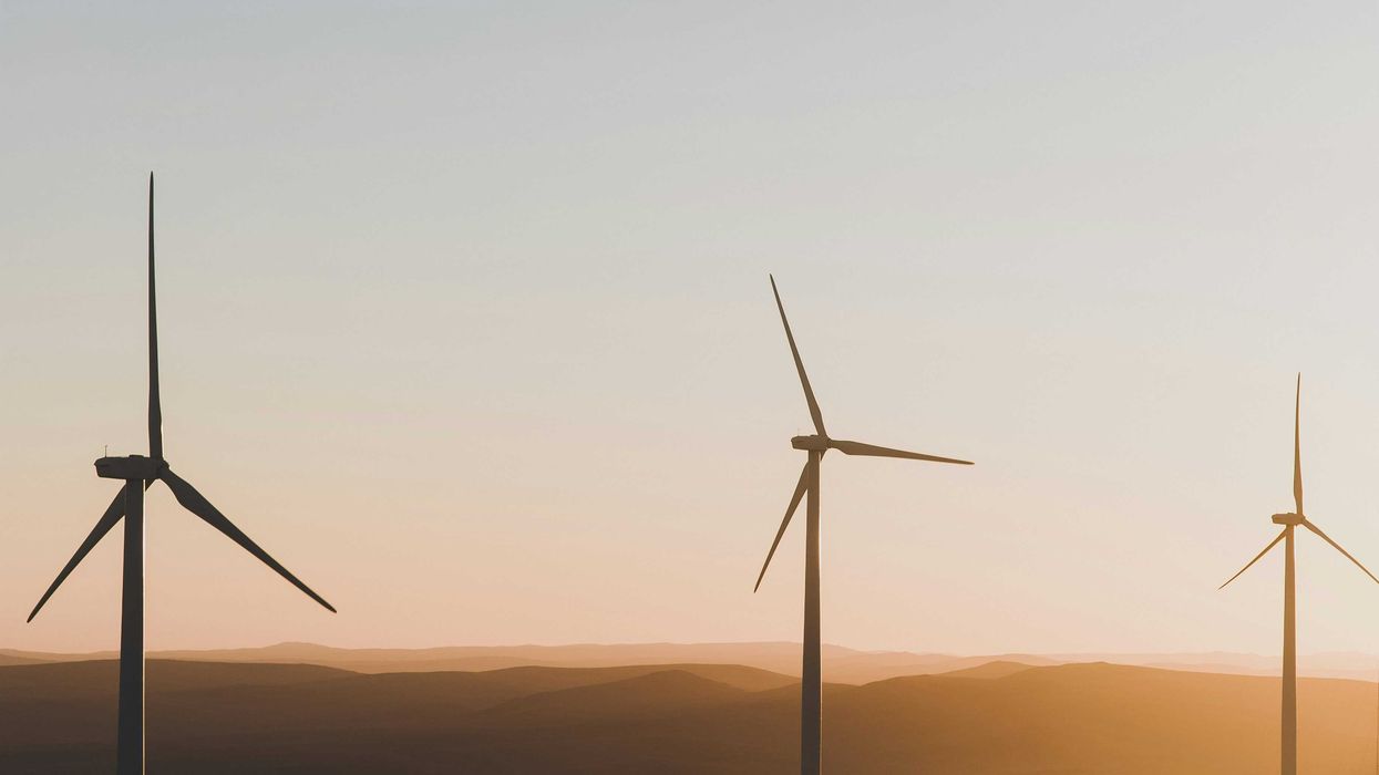 Wind turbines silhouetted against late afternoon sky with sun filtering over hills.