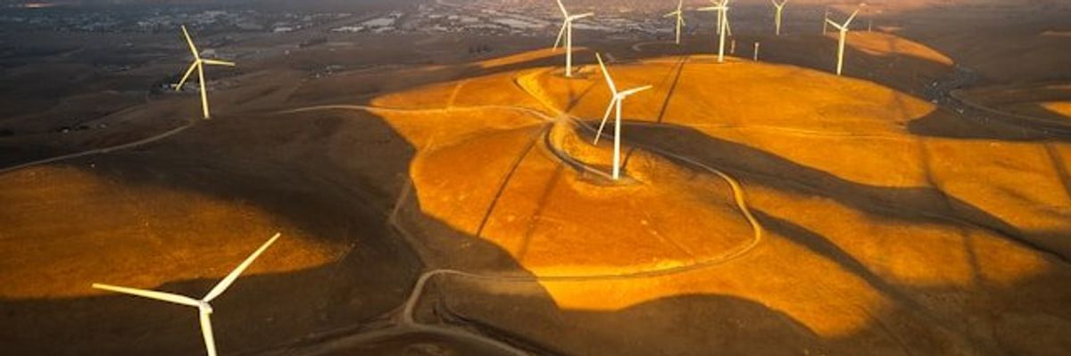 Wind turbines situated on dry hills above a valley.