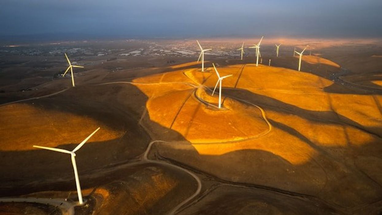 Wind turbines situated on dry hills above a valley.