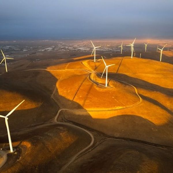 Wind turbines situated on dry hills above a valley.
