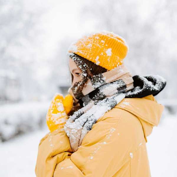 Woman bundled against cold, snowy weather wearing yellow coat andyellow hat.