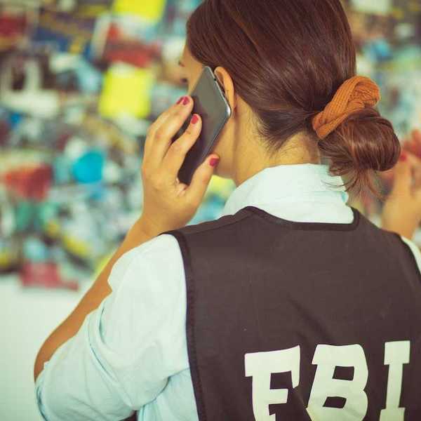 Woman FBI agent, back to camera, talking on the phone.