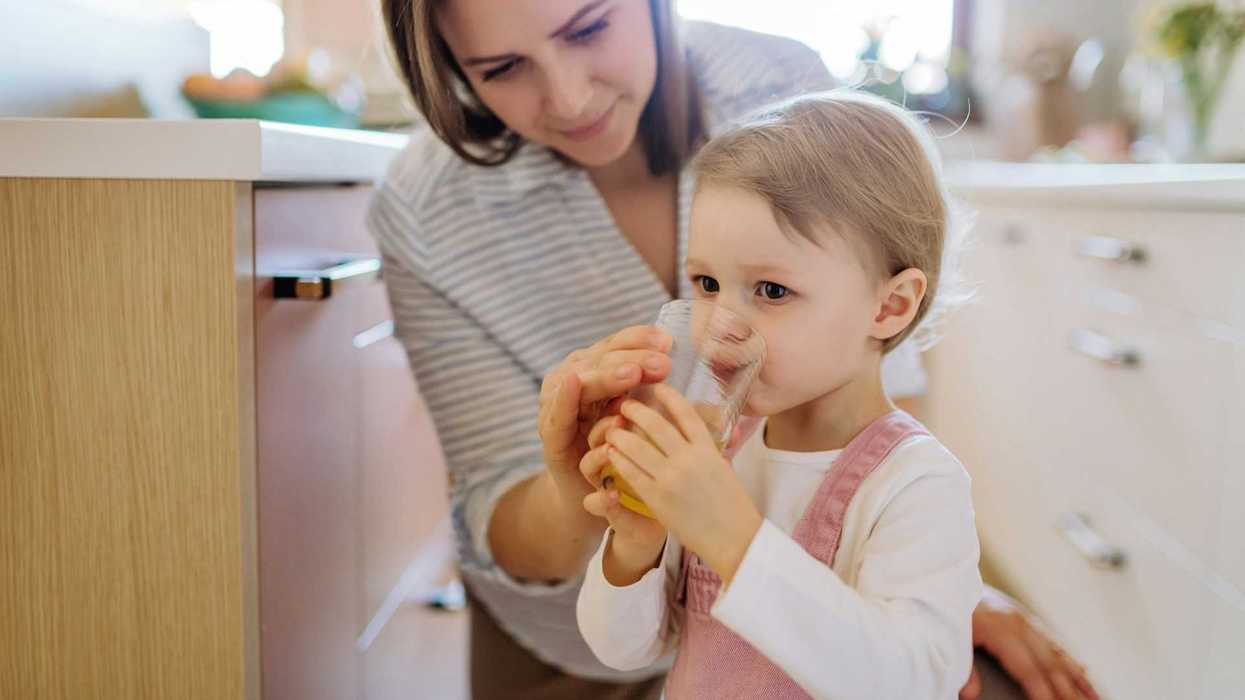 Woman helping toddler drink from a water glass