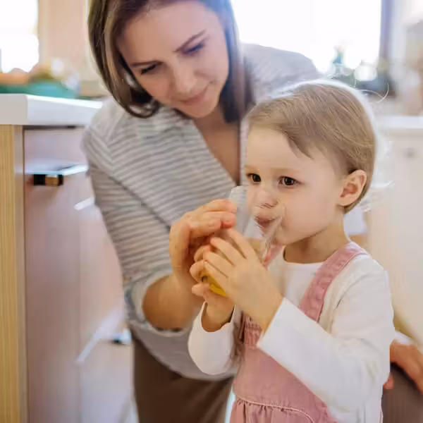 Woman helping toddler drink from a water glass