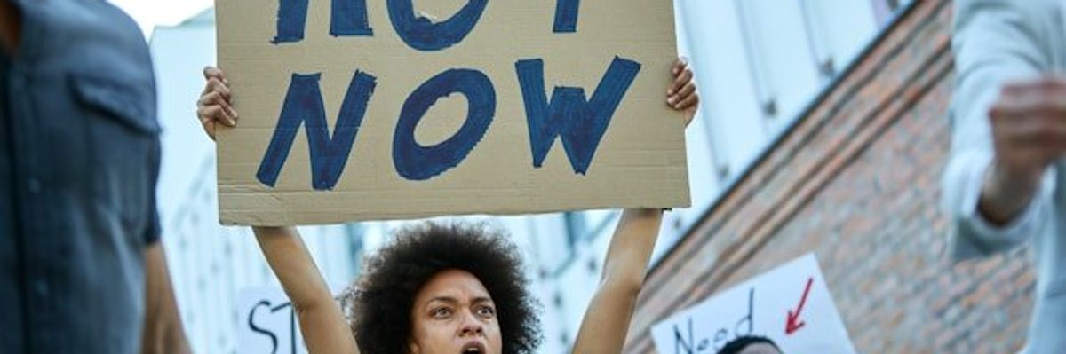 Woman holding a protest sign that says Act Now.