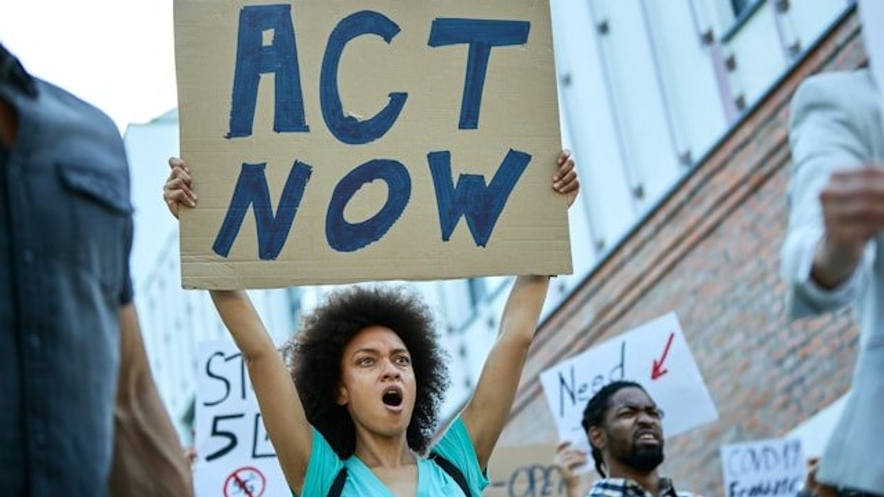 Woman holding a protest sign that says Act Now.