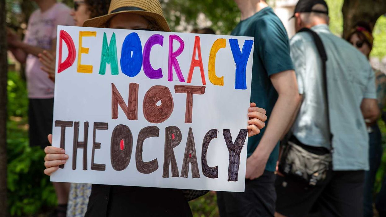 Woman holding sign reading: "Democracy Not Theocracy"