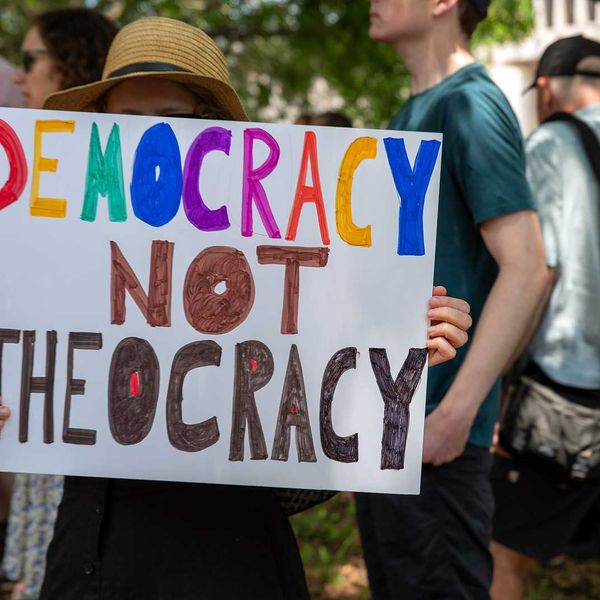 Woman holding sign reading: "Democracy Not Theocracy"