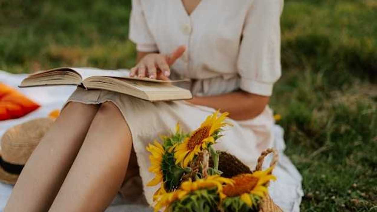 Woman in a summer dress reading a book next to a basket full of sunflowers