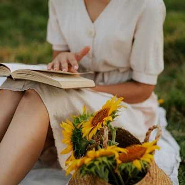 Woman in a summer dress reading a book next to a basket full of sunflowers