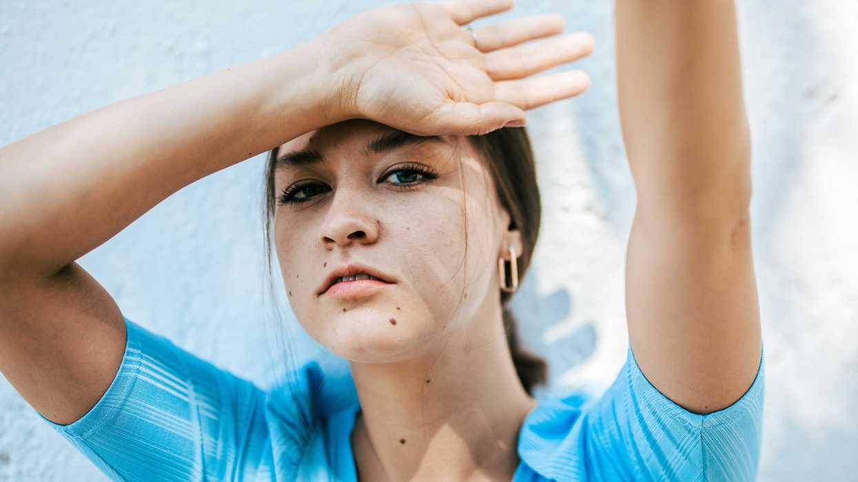woman in blue crew neck shirt with back of hand against forehead.