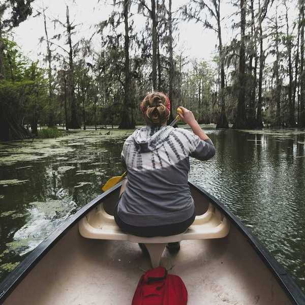 Woman in bow of canoe paddling in Bayou country shot from the stern of the canoe