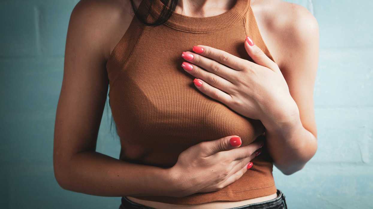Woman in brown tank top holding her chest in pain.