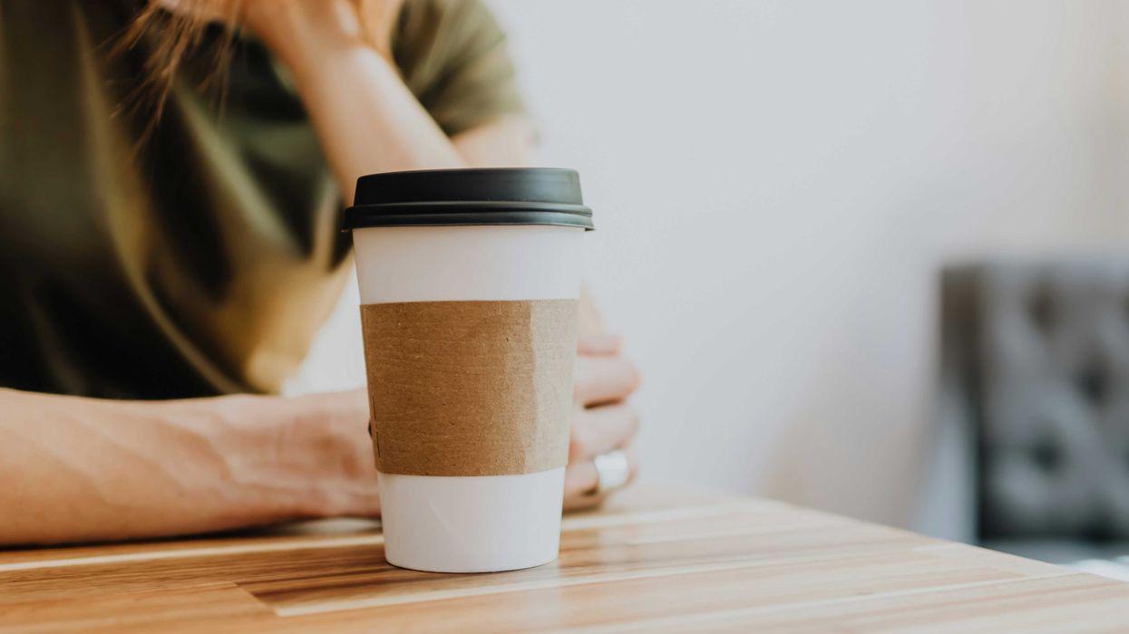 woman in green shirt holding white and black disposable cup.