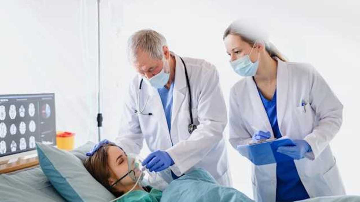 Woman in hospital bed wearing oxygen mask with two doctors leaning over her