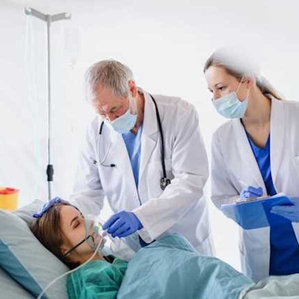 Woman in hospital bed wearing oxygen mask with two doctors leaning over her