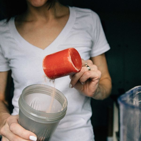 woman in white crew neck t-shirt holding red plastic cup with protein powder in it