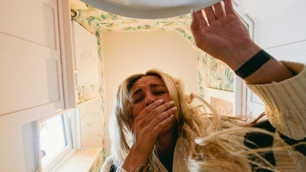 Woman lifting toilet seat and seemingly gagging at the sight and smell