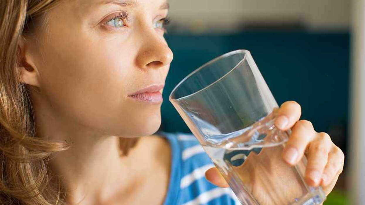 Woman looking into the distance thoughtfully while drinking a glass of water