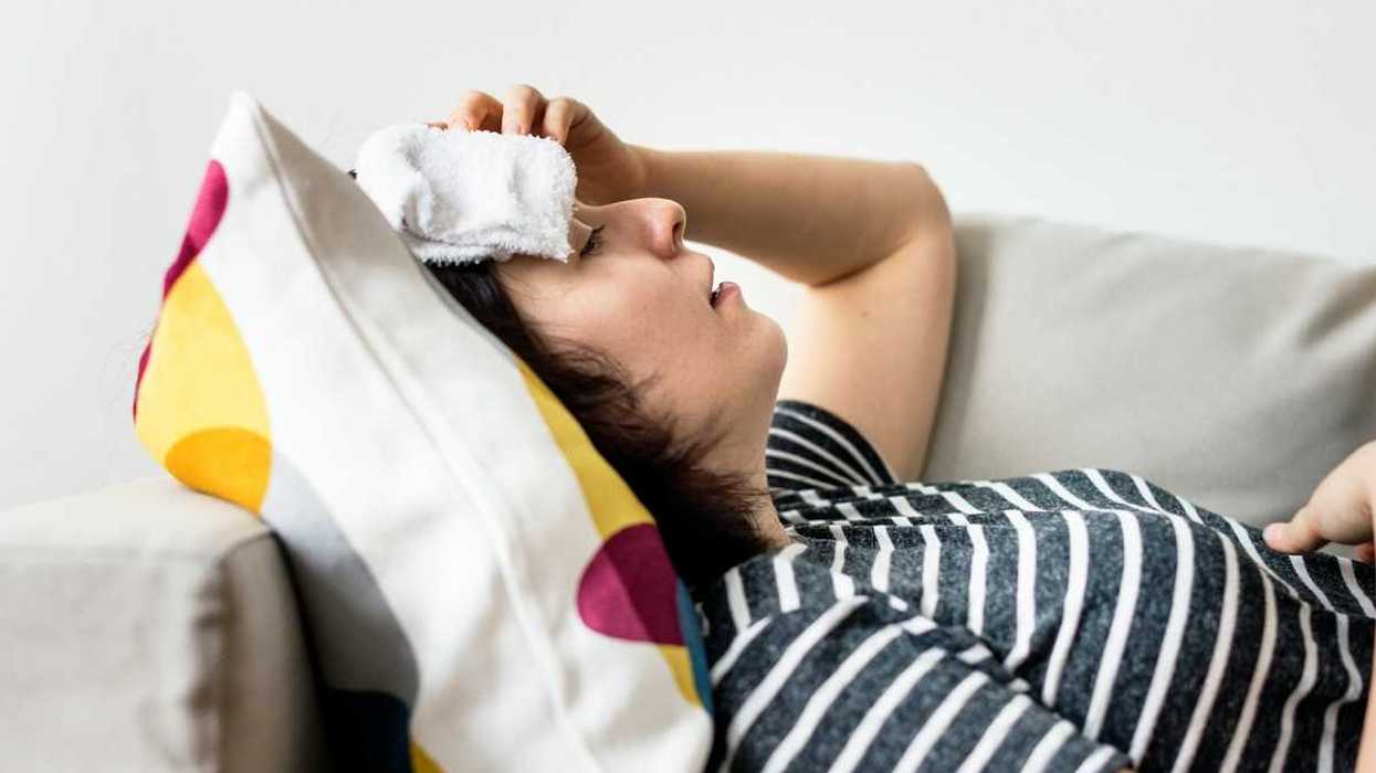 Woman, lying on a sofa with cold compress on forehead coping with extreme heat