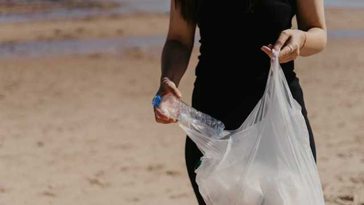 Woman placing a plastic bottle into a plastic bag on a beach