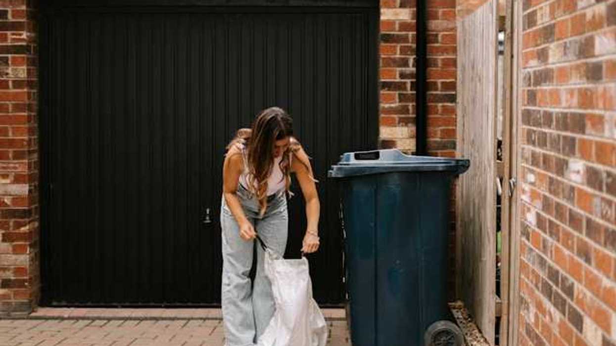 Woman placing a plastic trash bag on the grown next to a trash bin
