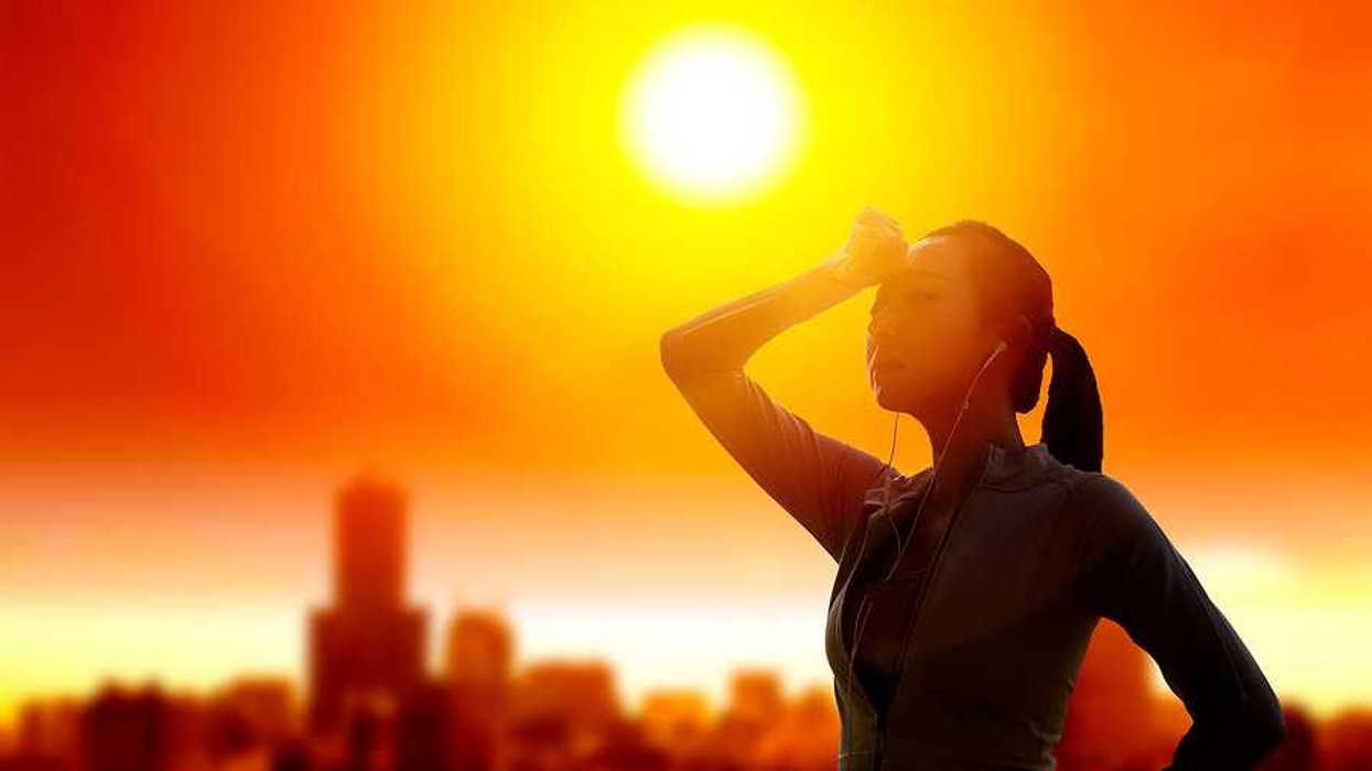Woman shielding her eyes from sun with summer heat wave in the city background.